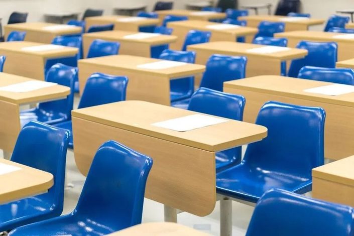 Aula vuota con file di banchi in legno chiaro e sedie blu