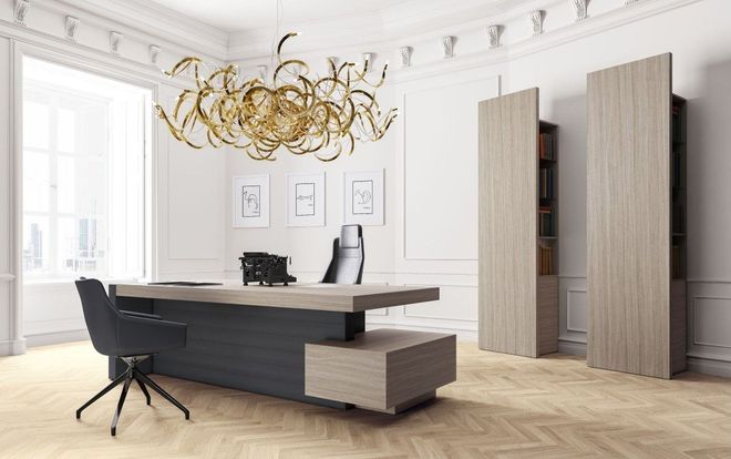 Ufficio moderno bianco con scrivania scura, sedia nera, lampadario dorato e armadi alti.