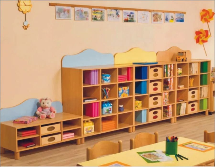 Aula colorata con scaffali in legno, giocattoli e tavolini bassi su un pavimento in legno chiaro