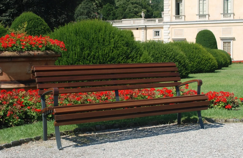 Panchina di legno accanto a fiori rossi e arbusti verdi in un cortile con giardino