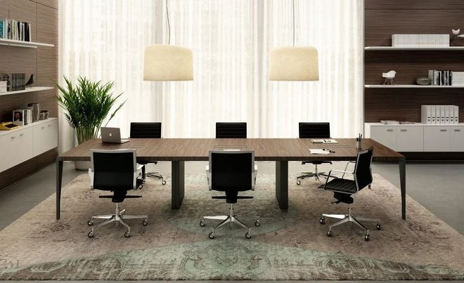 Moderna sala conferenze con un lungo tavolo, sedie da ufficio nere e lampade a sospensione sopra un tappeto.