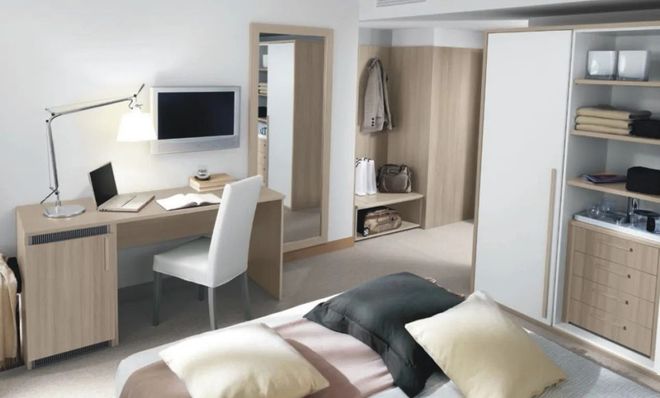 Camera da letto moderna con scrivania, sedia, monitor a parete, armadio aperto e letto ben rifatto