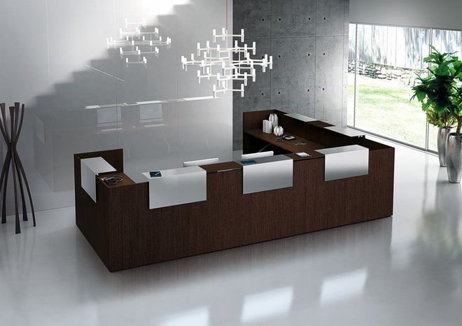 Reception moderna in una luminosa hall con sedie bianche, banconi in legno scuro e una lampada a sospensione.
