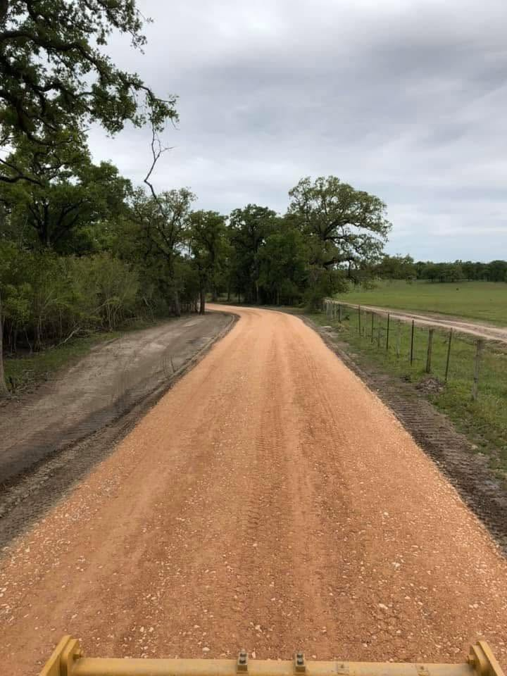 Curving dirt road through green fields and trees under an overcast sky