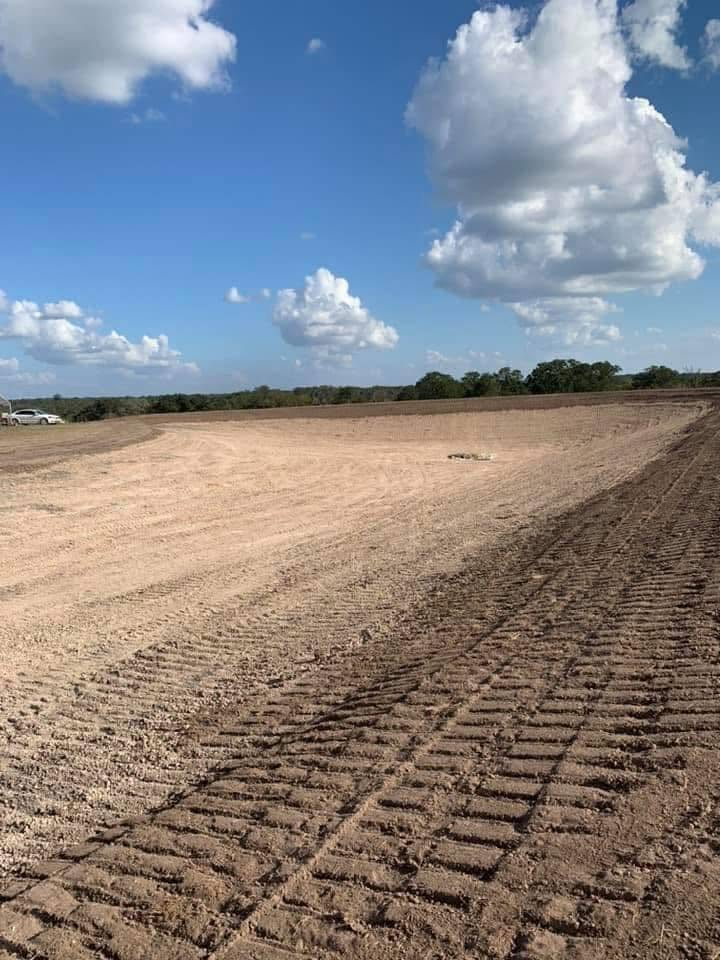 Wide sandy construction site under a blue sky with scattered clouds and tire tracks in the foreground
