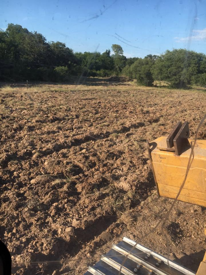 Freshly plowed dirt field with trees along the edge and a yellow farm machine in the foreground.