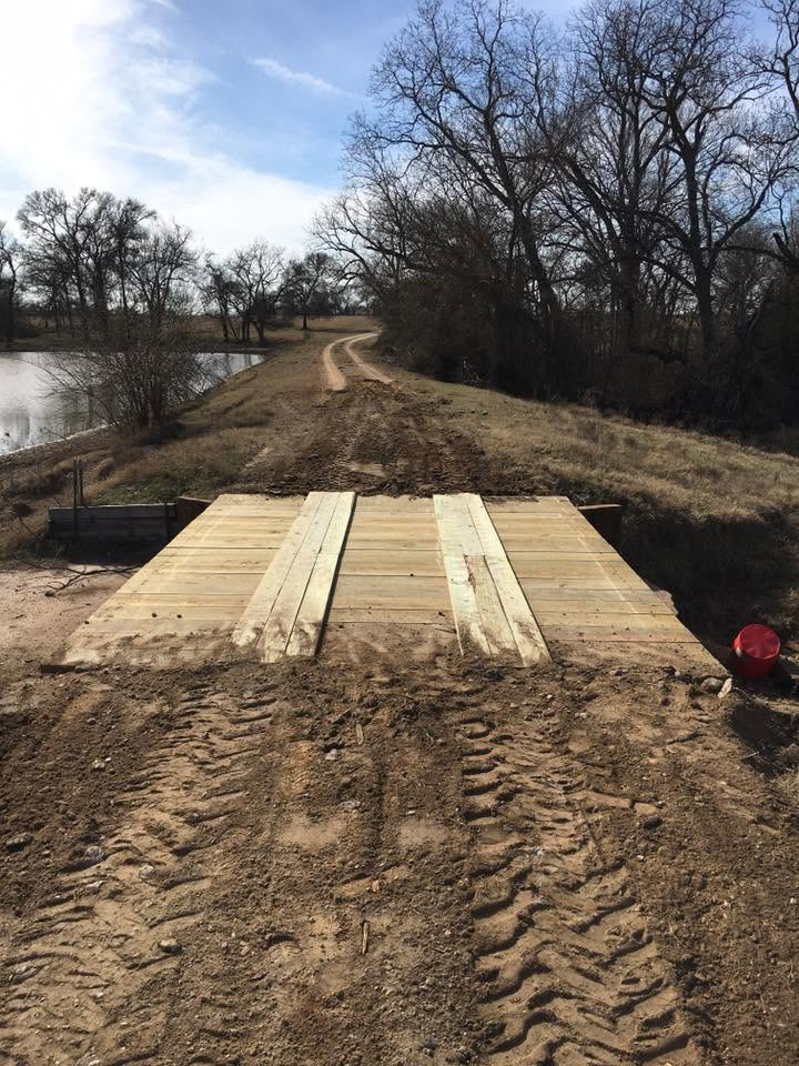 Temporary wooden ramp over a muddy dirt path beside a river under bare trees