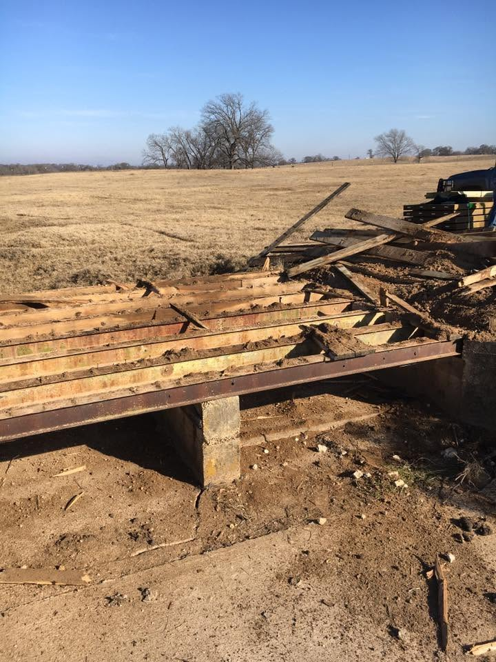 Collapsed wooden deck in a dry rural field under a clear blue sky.