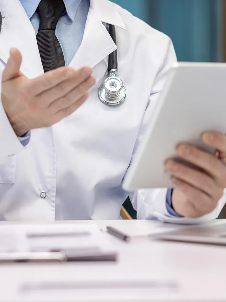 Doctor in white coat holding a tablet and gesturing in a medical office