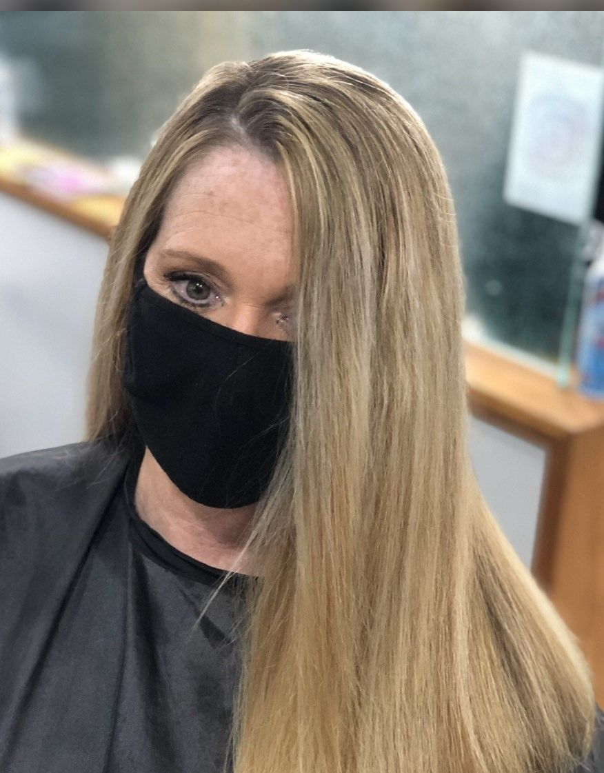 Woman with blonde hair wearing a black face mask, in a salon.