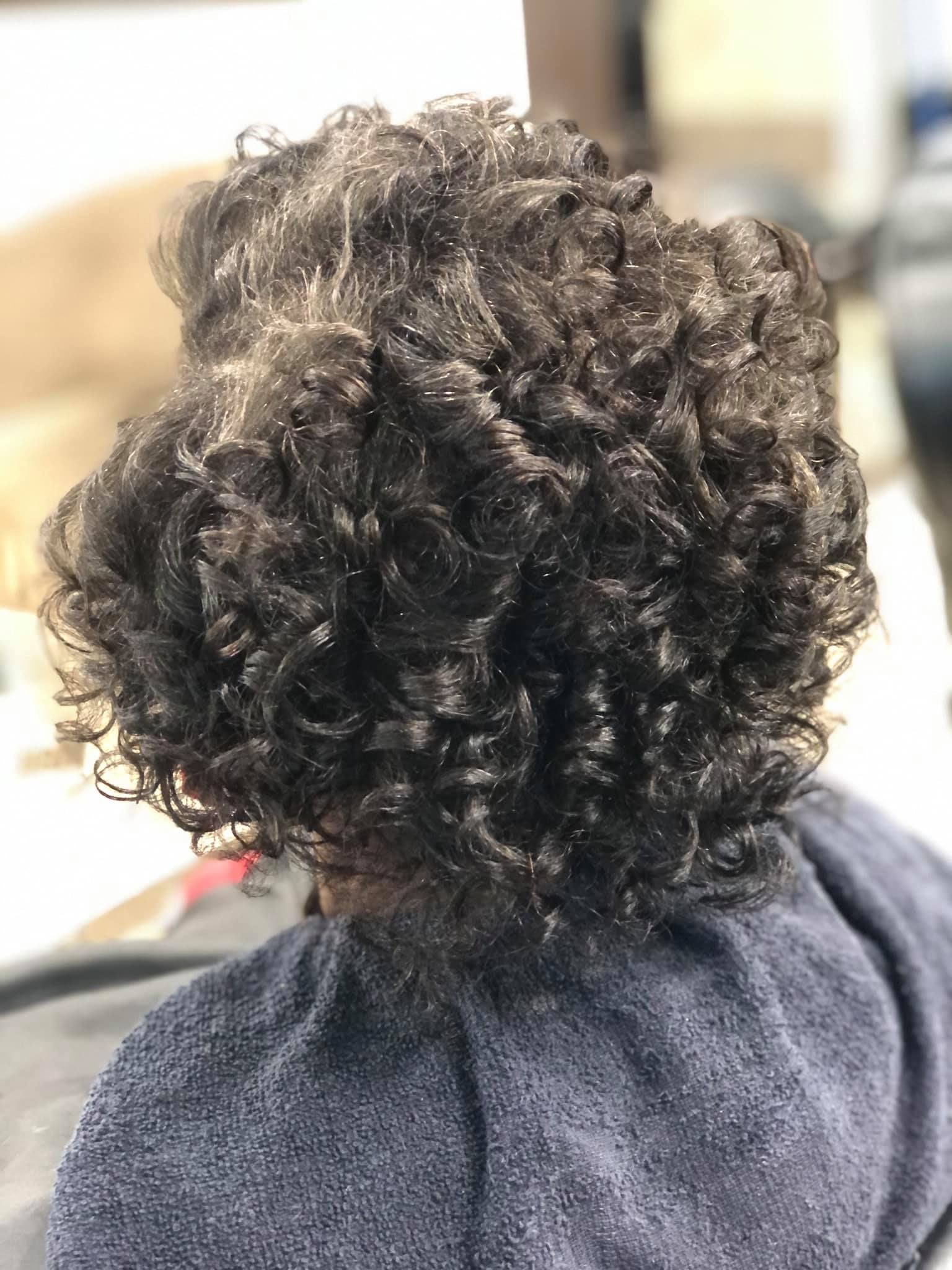 Close-up of curly dark hair styled on a person's head, possibly in a salon setting.