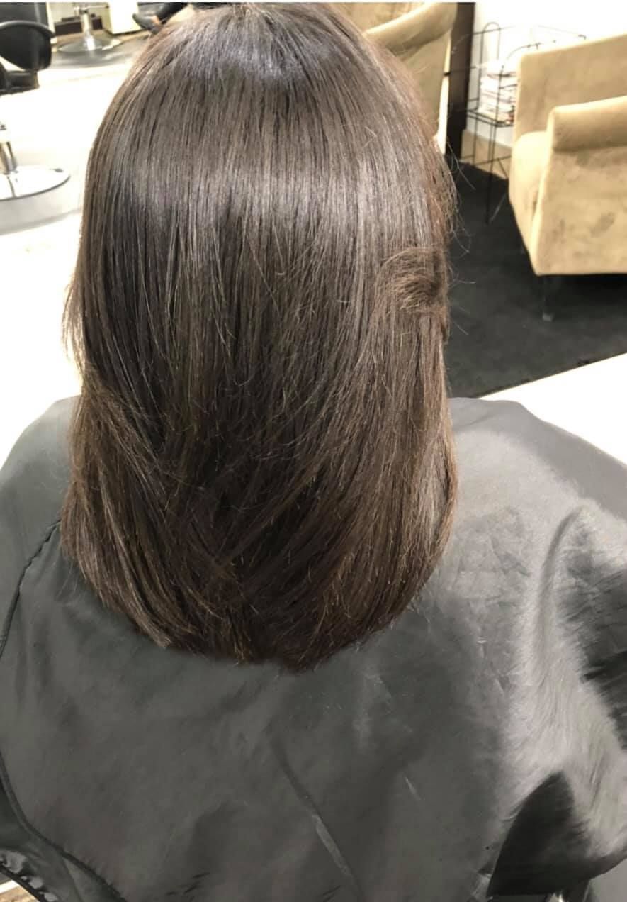 Person with layered dark brown hair in a salon chair, looking down.