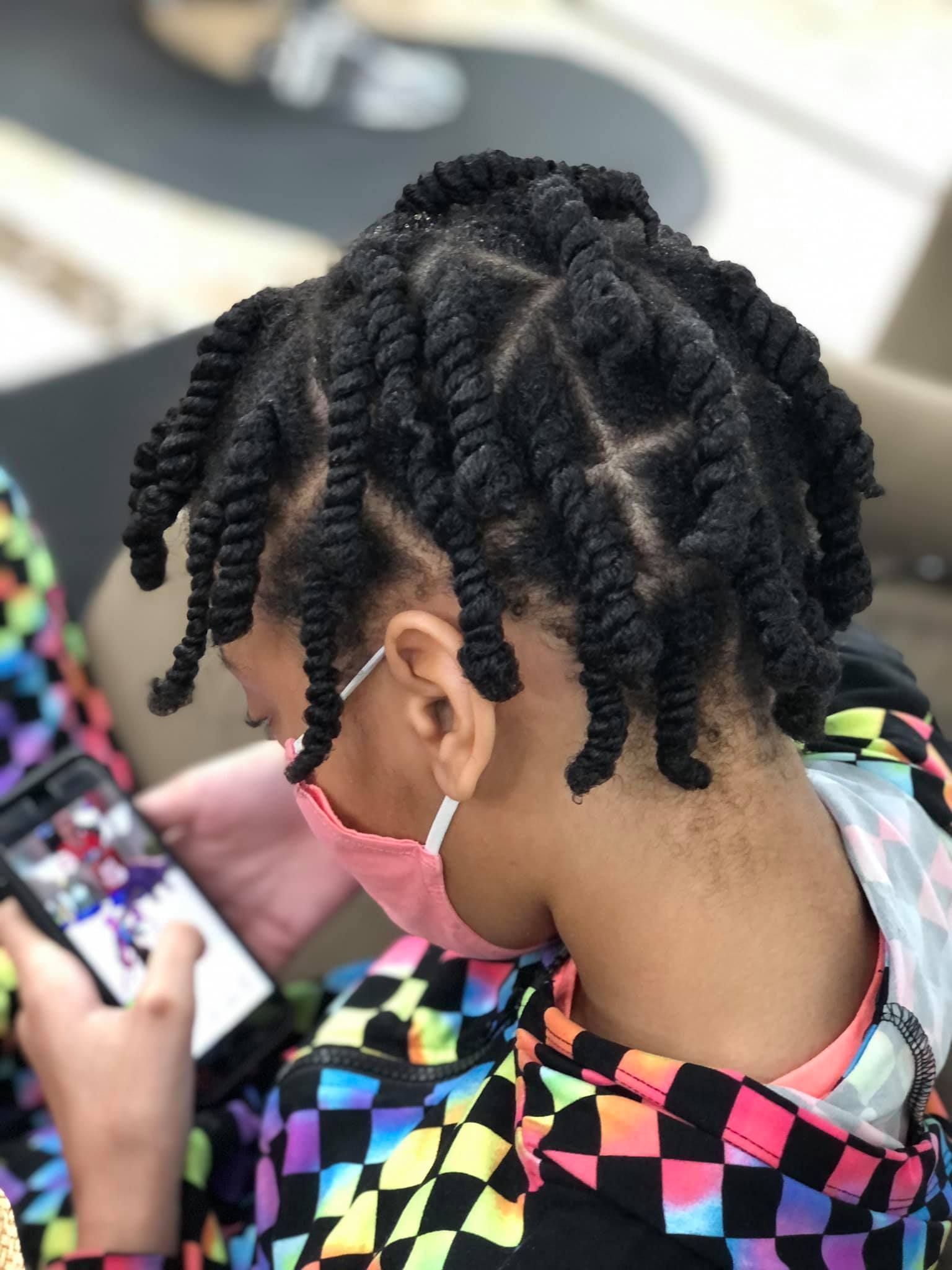 Child with protective twists, wearing a mask, looking at a phone, in a colorful jacket.