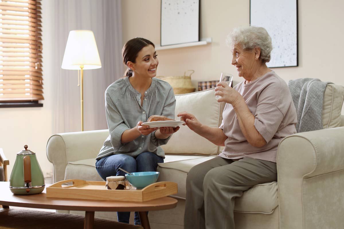 A woman is giving an elderly woman a gift while they are sitting on a couch.