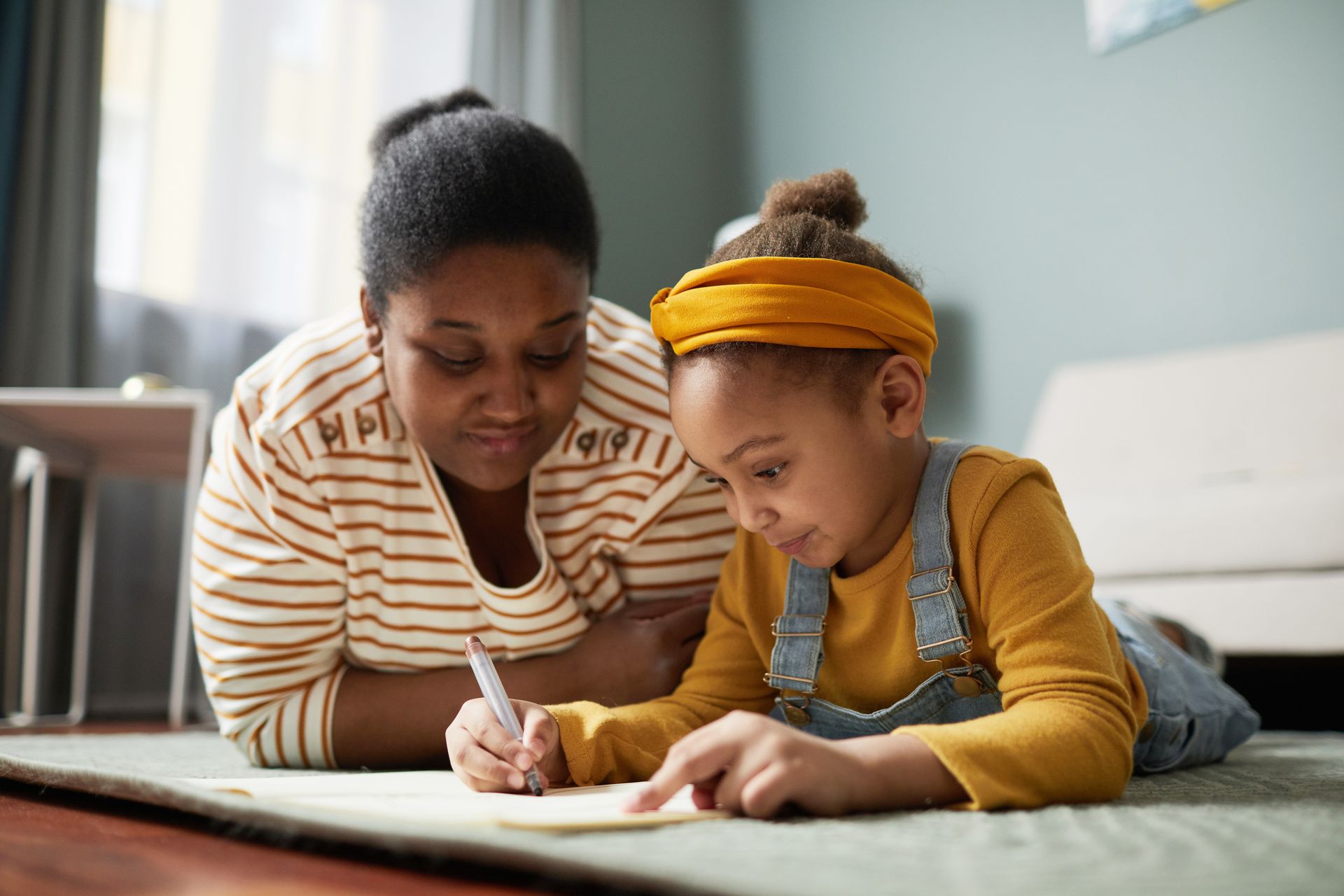 a woman and a little girl are laying on the floor writing in a notebook