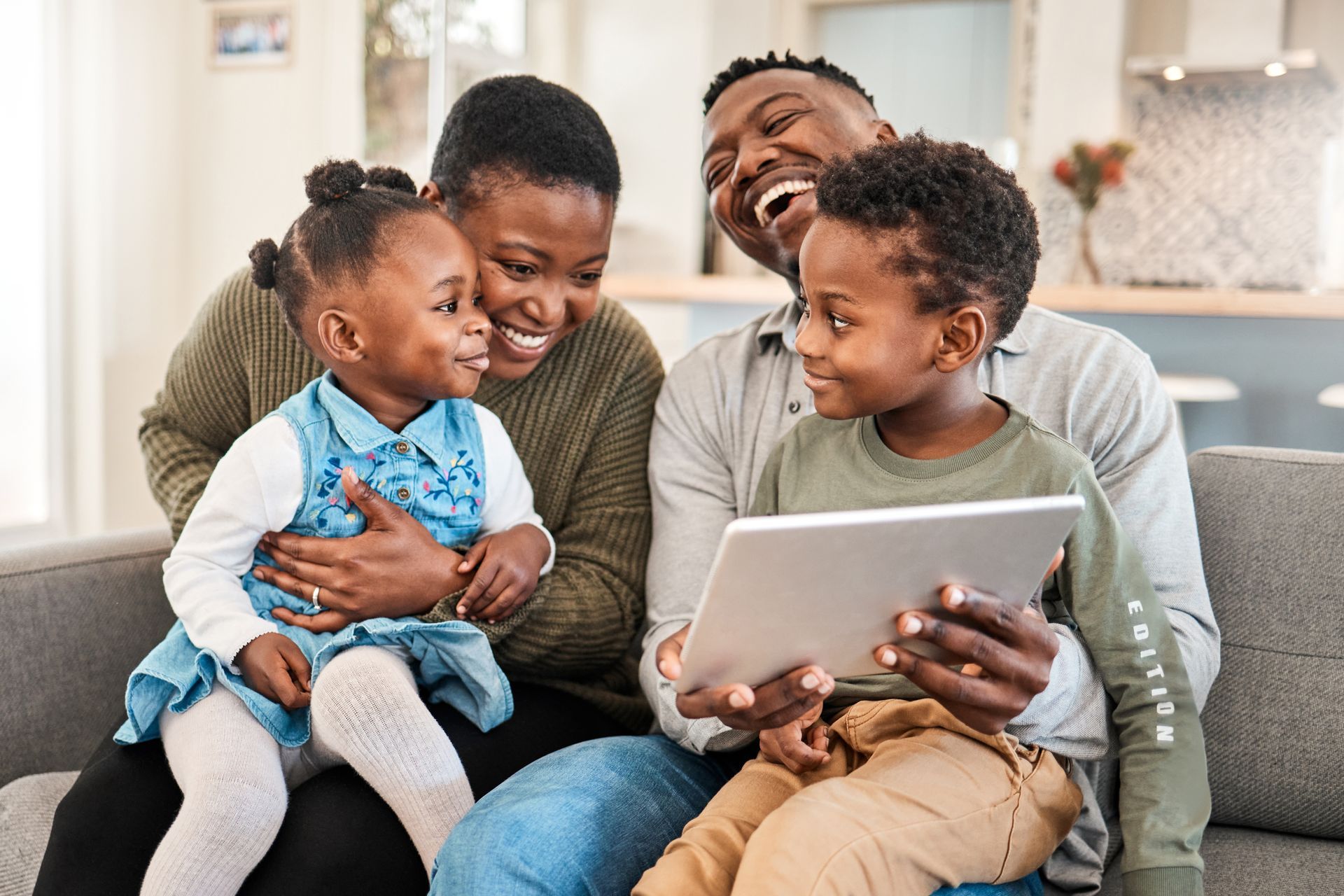 a family is sitting on a couch looking at a tablet