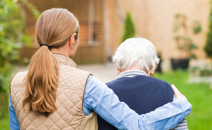 Woman assisting an elderly person outdoors near a building