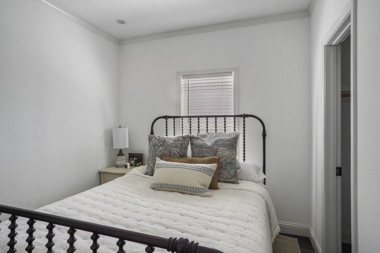Perpetual Homes ADU: Small bedroom with a wrought iron bed, white walls, and a window.