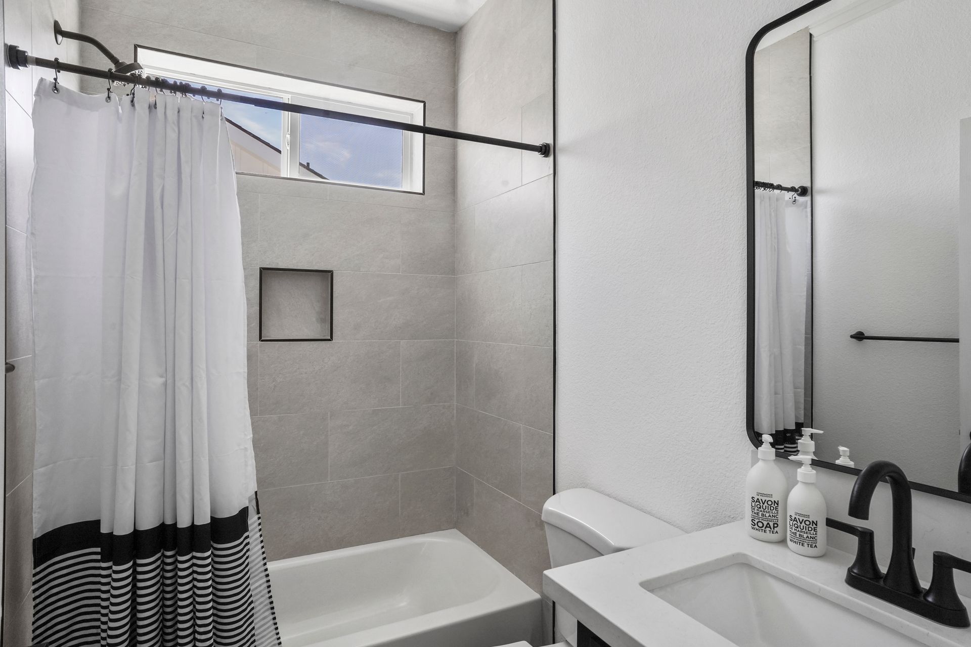 Perpetual Homes ADU: Bathroom with white tub and sink, black-framed mirror, and shower curtain with black stripes.