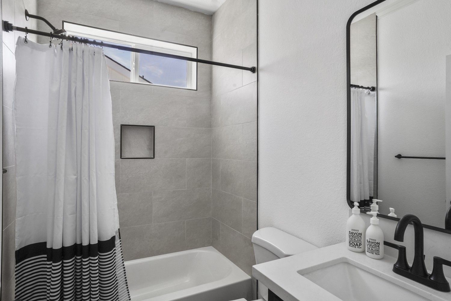 Perpetual Homes ADU: Bathroom with a bathtub, shower curtain, sink, mirror, and toilet.