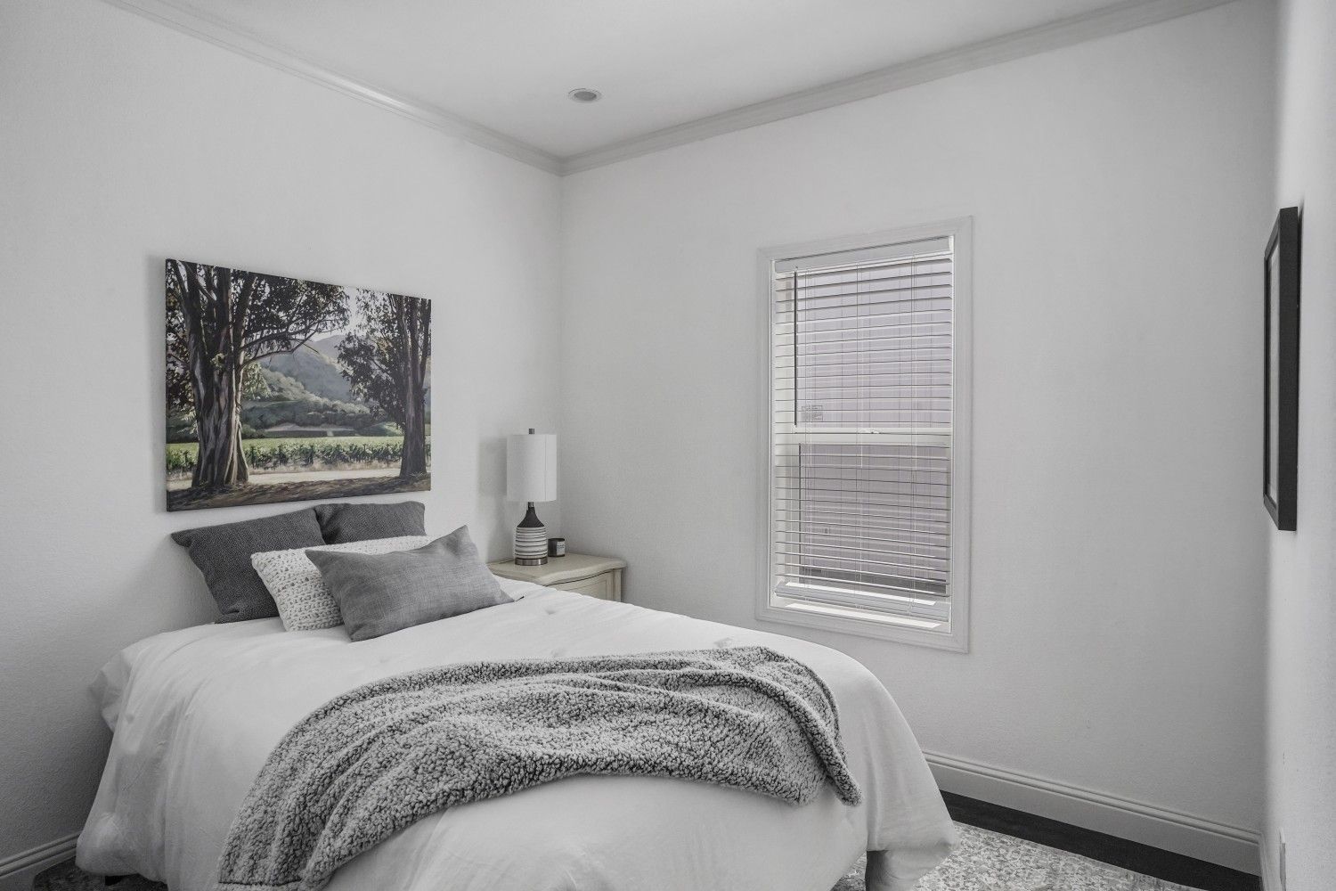 Perpetual Homes ADU: Bedroom with white walls, a bed with gray bedding, a landscape picture, and a window.