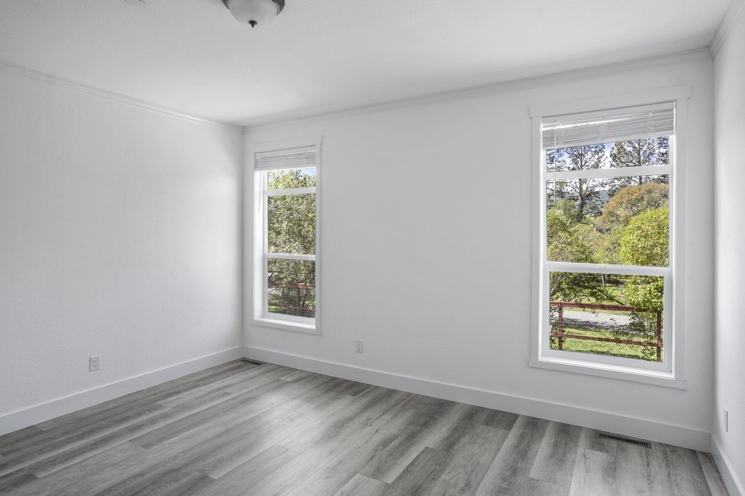 Perpetual Homes ADU: Empty room with two windows, white walls, gray wood floor, and natural outdoor view.