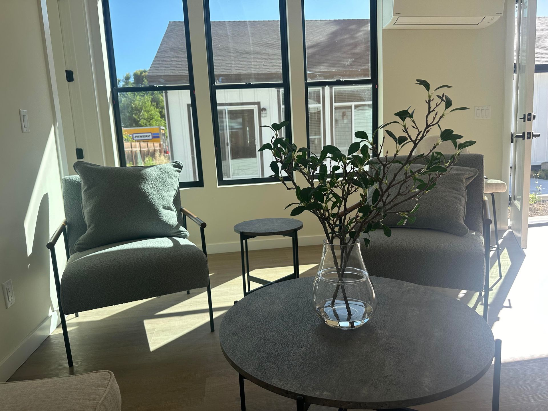 Perpetual Homes ADU: Living room with two gray armchairs, a round coffee table, and a glass vase with branches. Window view.