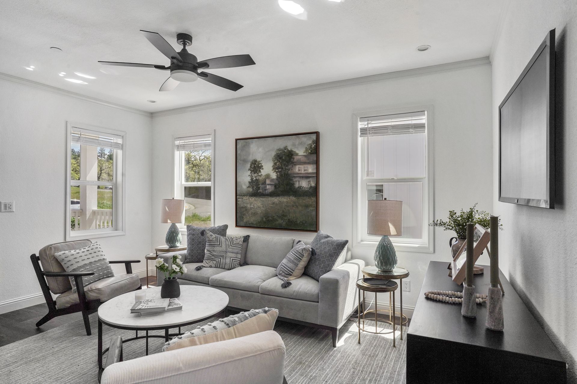 Perpetual Homes ADU: Living room with gray sofa, armchairs, coffee table, art, TV, windows, ceiling fan.