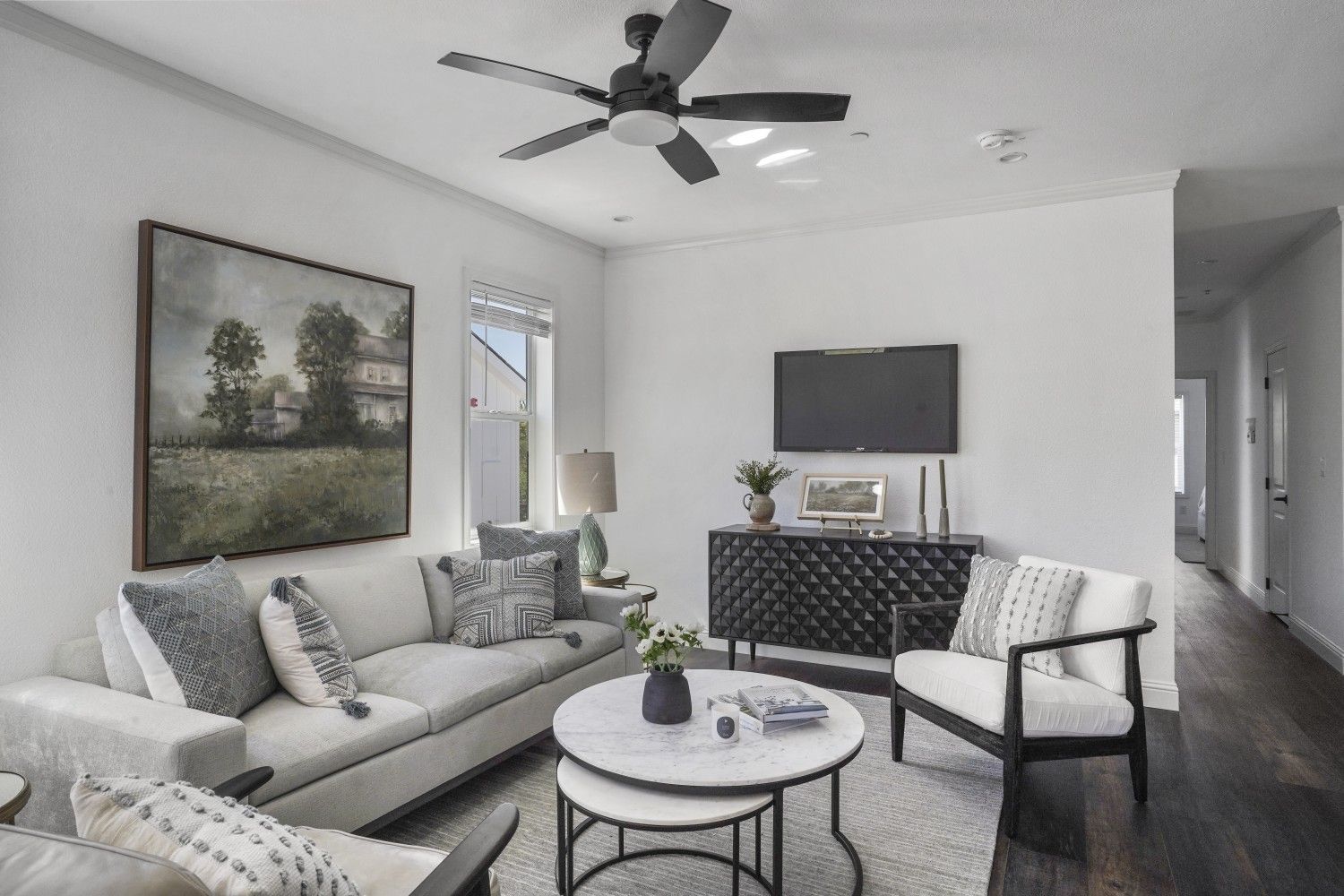 Perpetual Homes ADU: Living room with white walls, sofa, TV, and black ceiling fan.