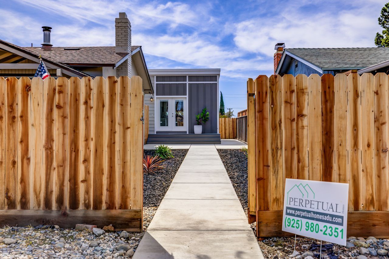 Perpetual Homes ADU: A gray modern home with a white door, accessed by a concrete path through a wooden fence.