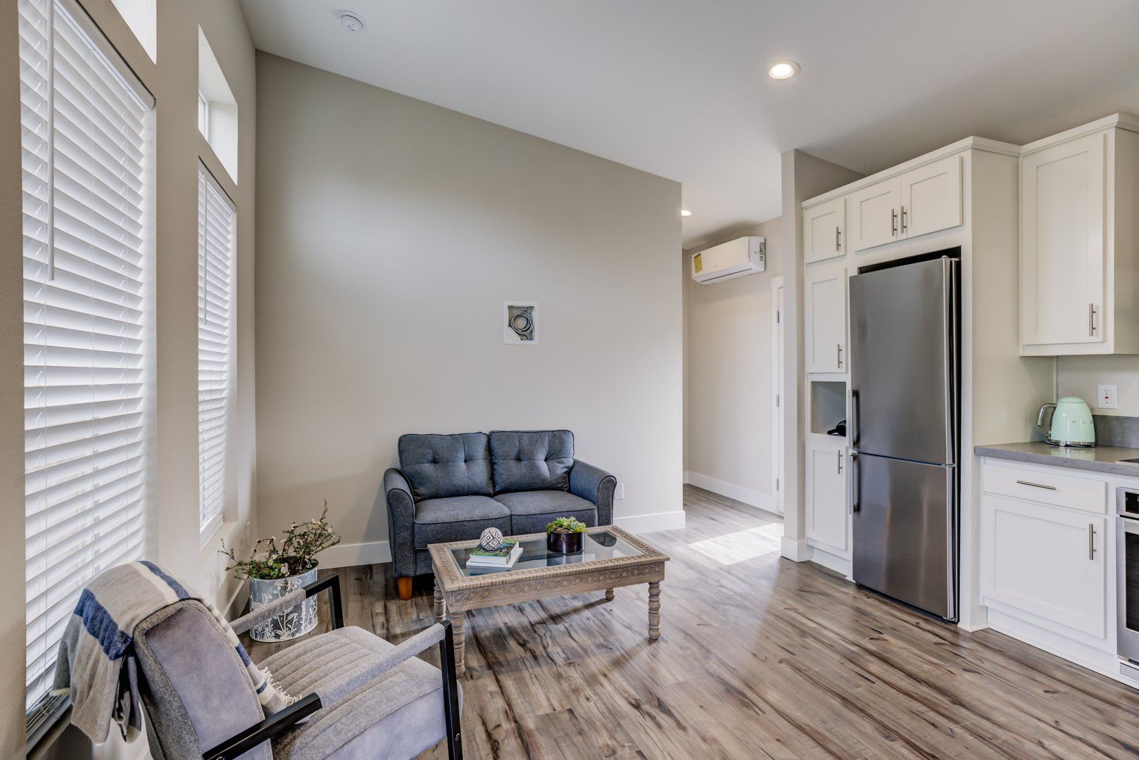 Perpetual Homes ADU: Living room and kitchen combo with a gray couch, stainless steel fridge, and wood floors.