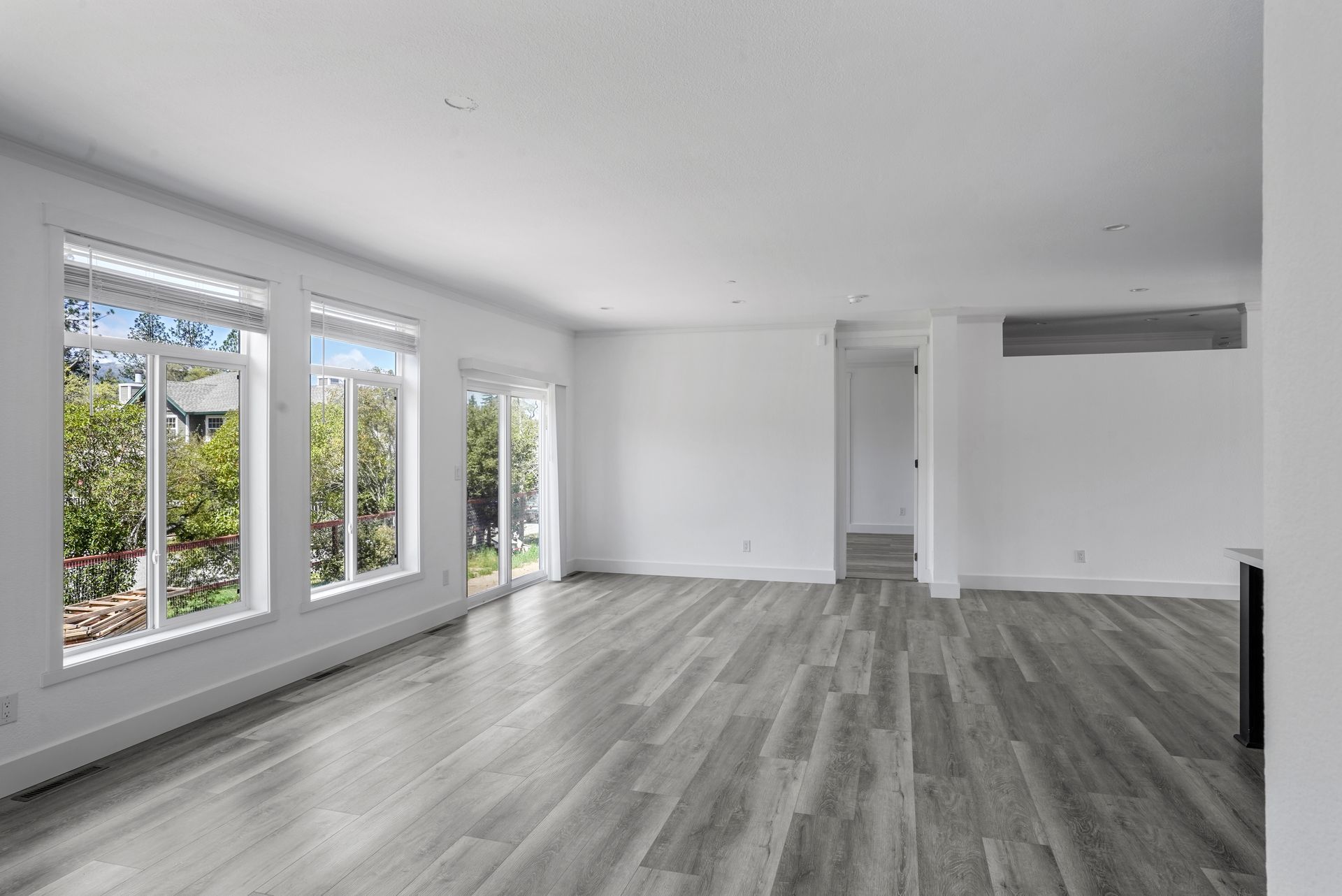 Perpetual Homes ADU: Empty, modern living room with gray wood floors, large windows, and white walls.