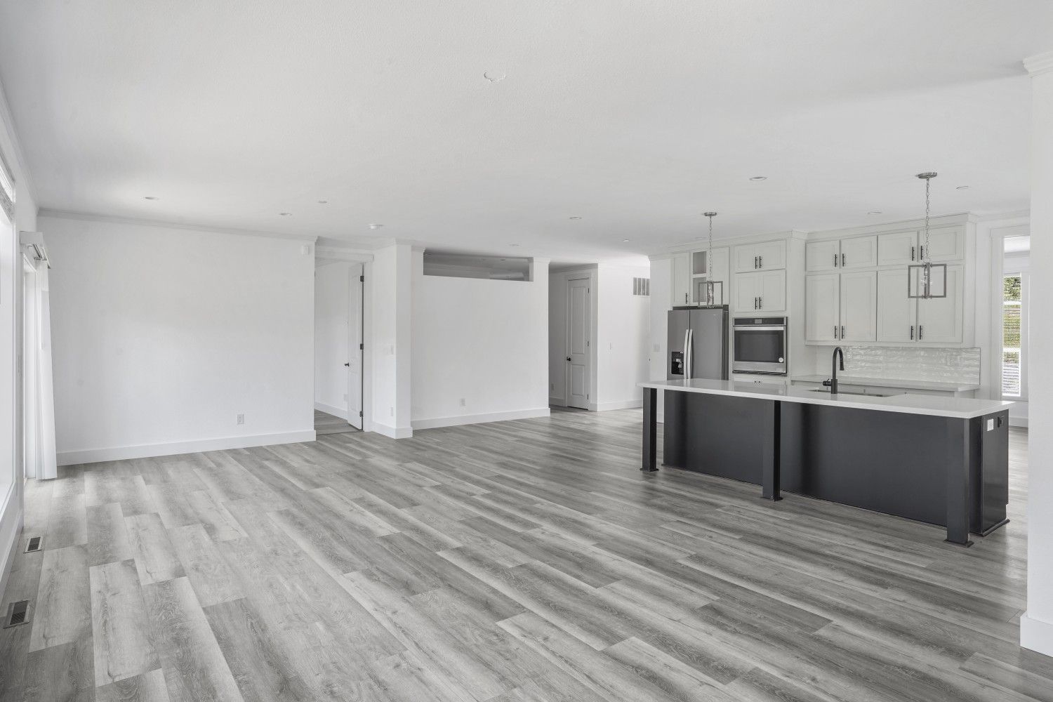 Perpetual Homes ADU: Empty open-concept living space with gray flooring, white walls, and kitchen island with white cabinets.