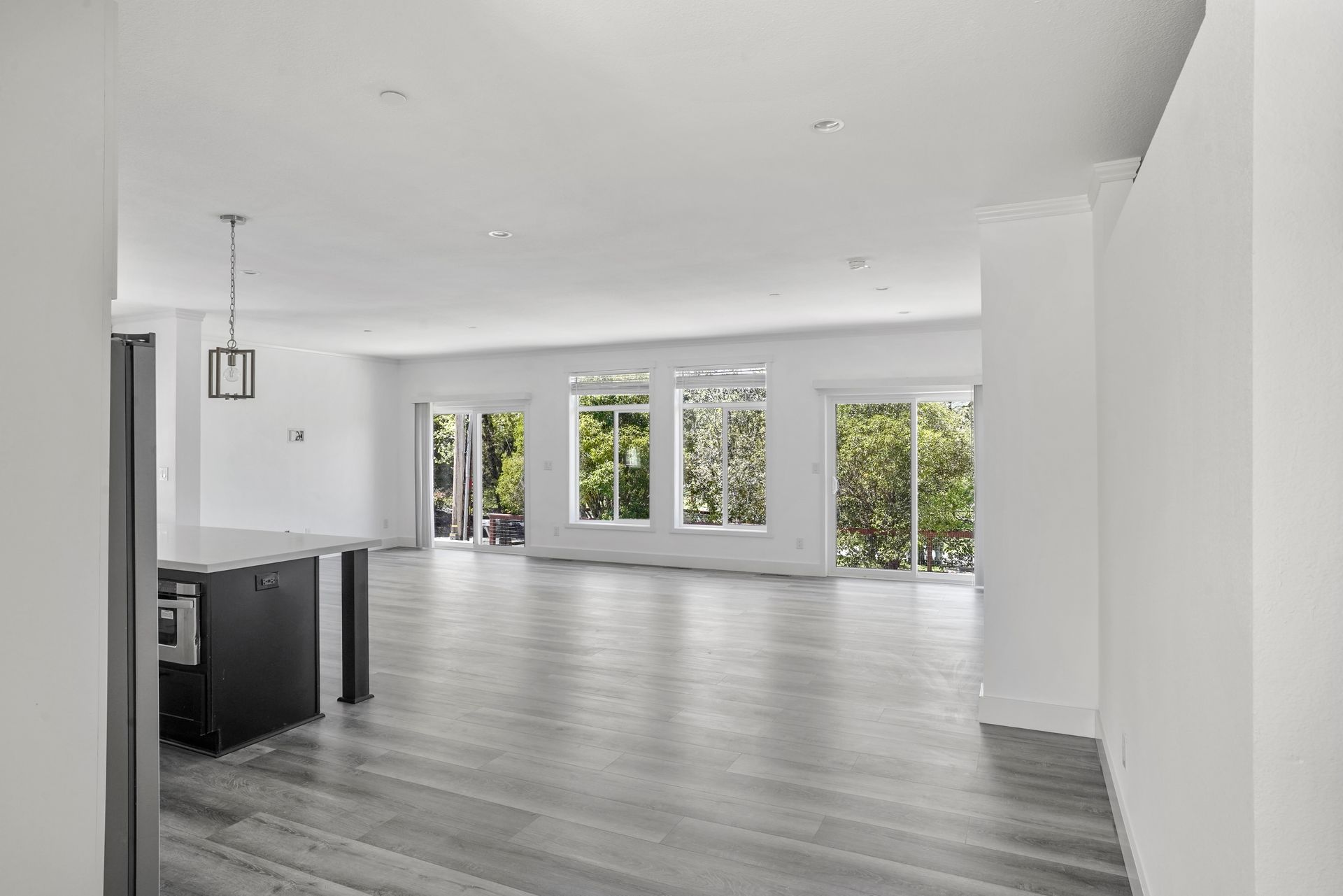 Perpetual Homes ADU: Empty, bright living area with gray floors, large windows, and a dark kitchen island.