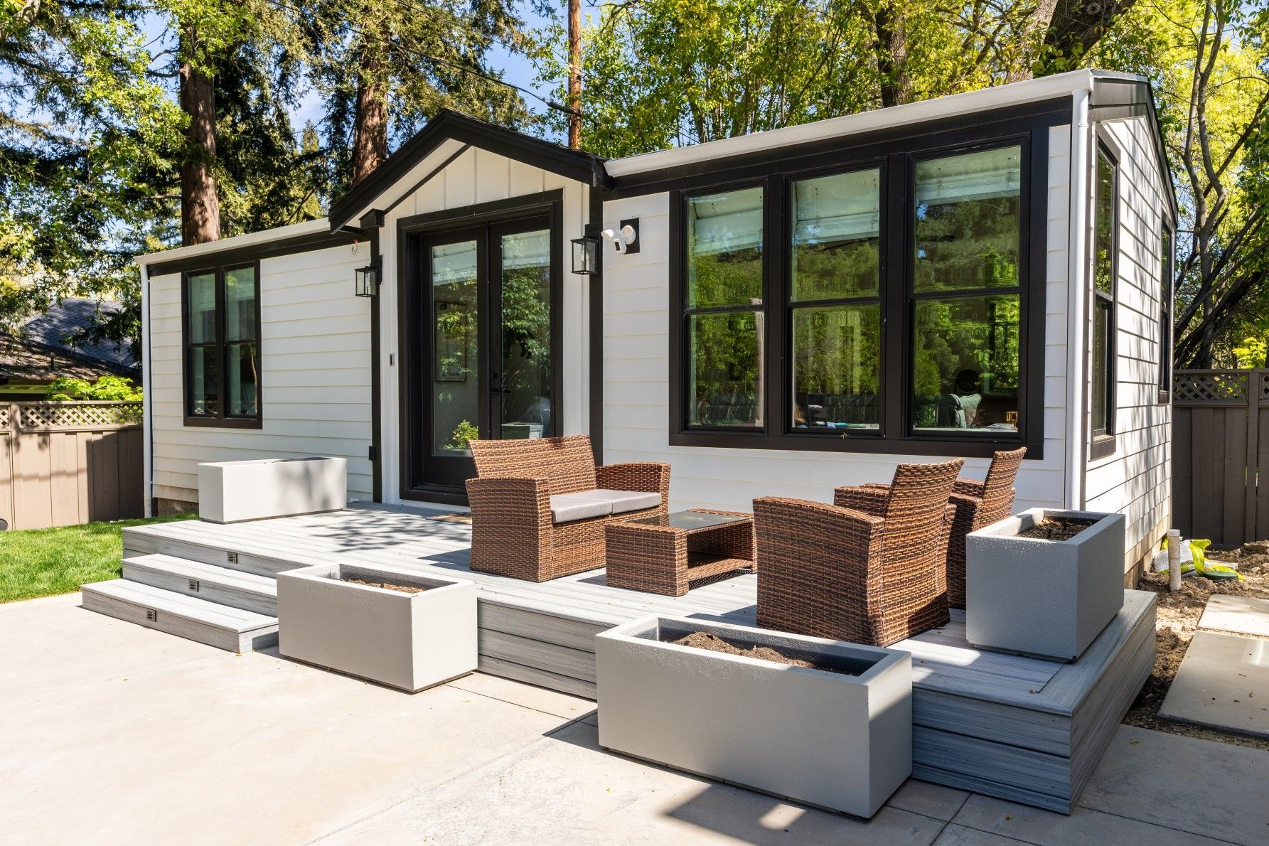Perpetual Homes ADU: White cottage house with black trim, patio furniture, and concrete planters.