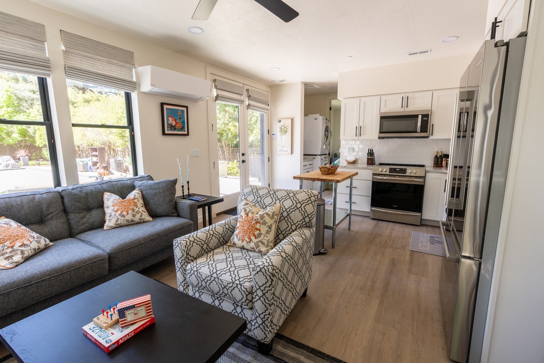 Perpetual Homes ADU: Open-concept living space with gray sofa, patterned chair, and white kitchen with hardwood floors.
