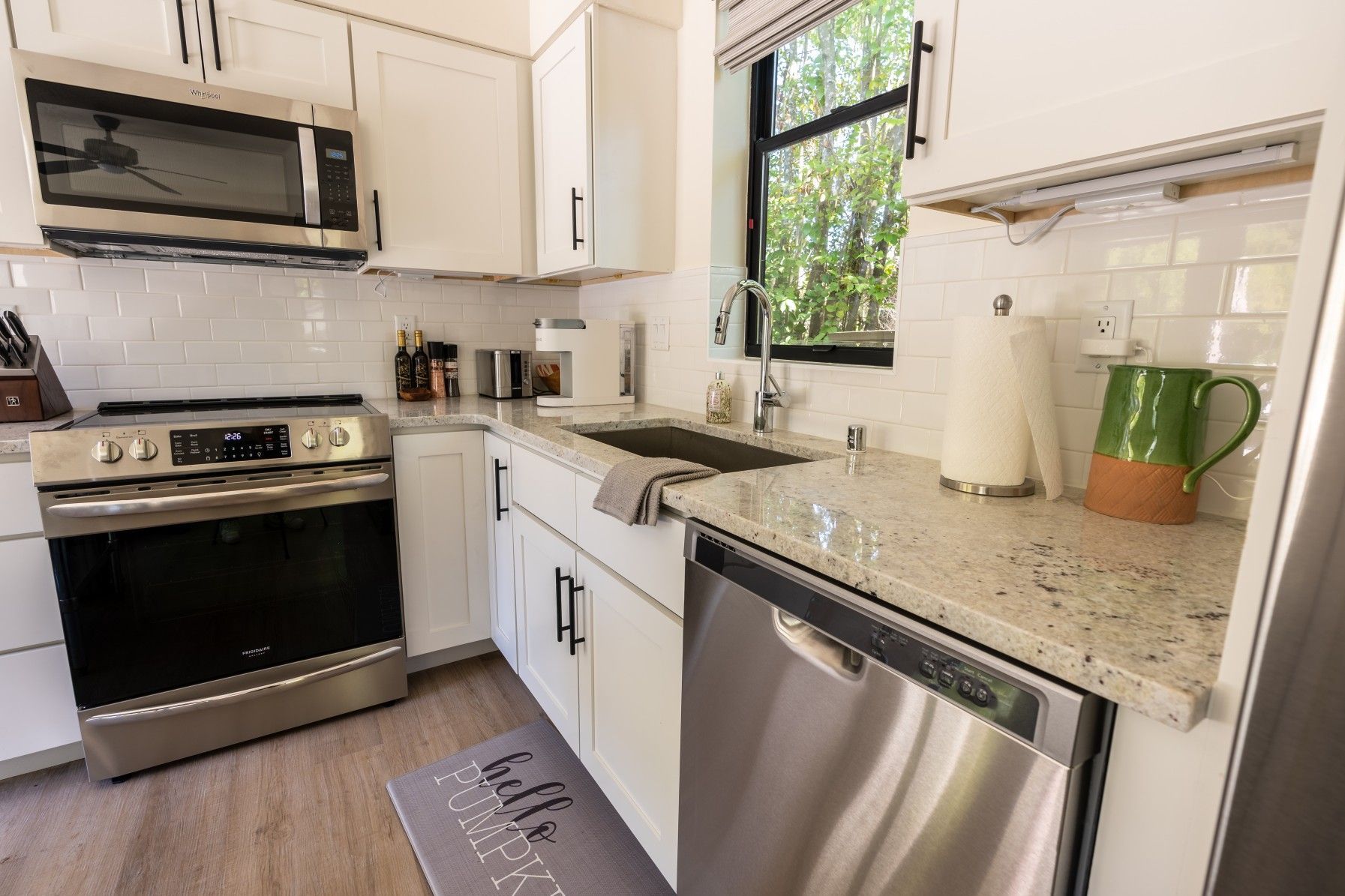 Perpetual Homes ADU: White kitchen with stainless steel appliances, white cabinets, and speckled countertops.