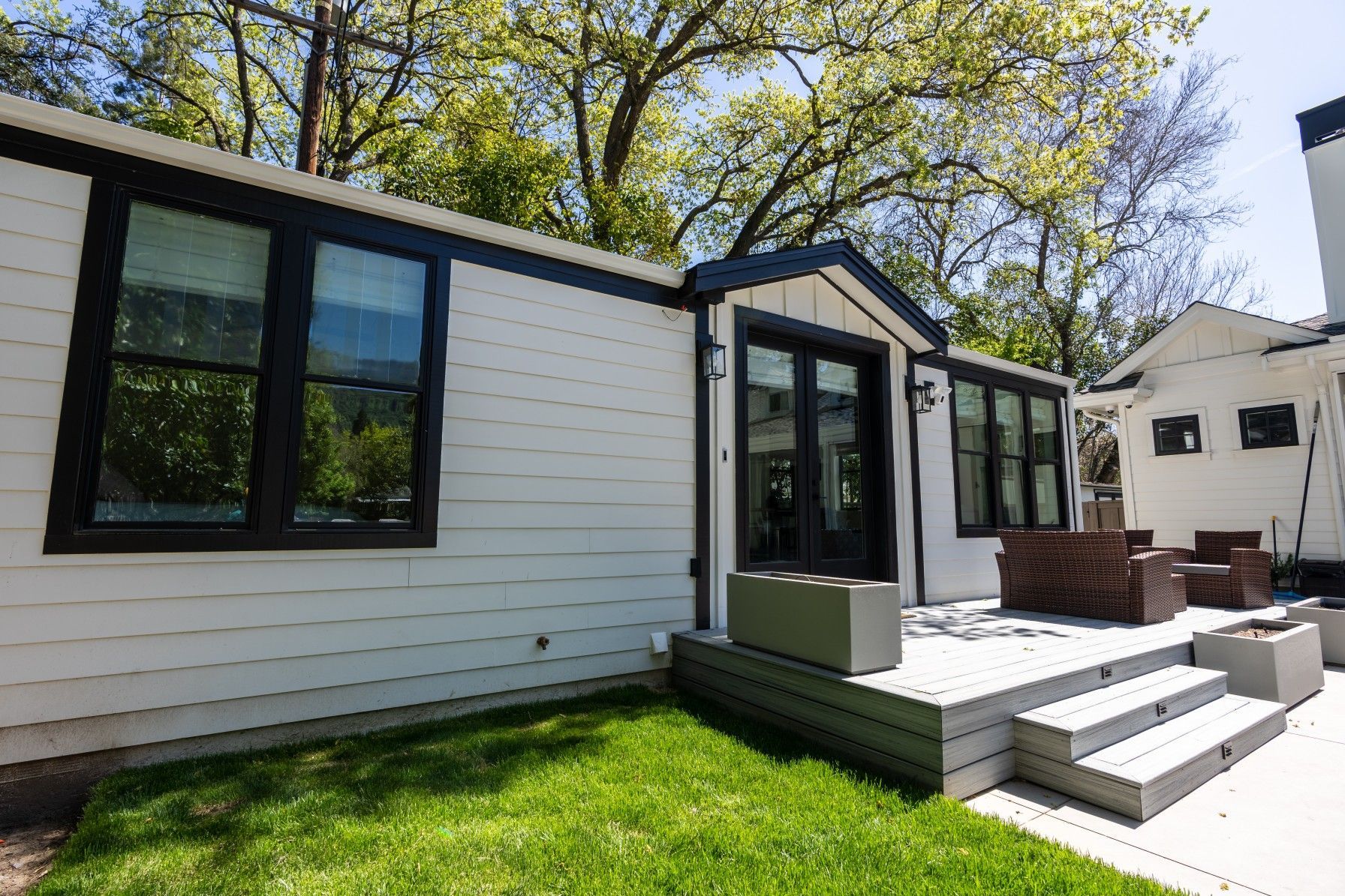 Perpetual Homes ADU: White backyard house exterior with black trim, patio, green lawn, and trees.