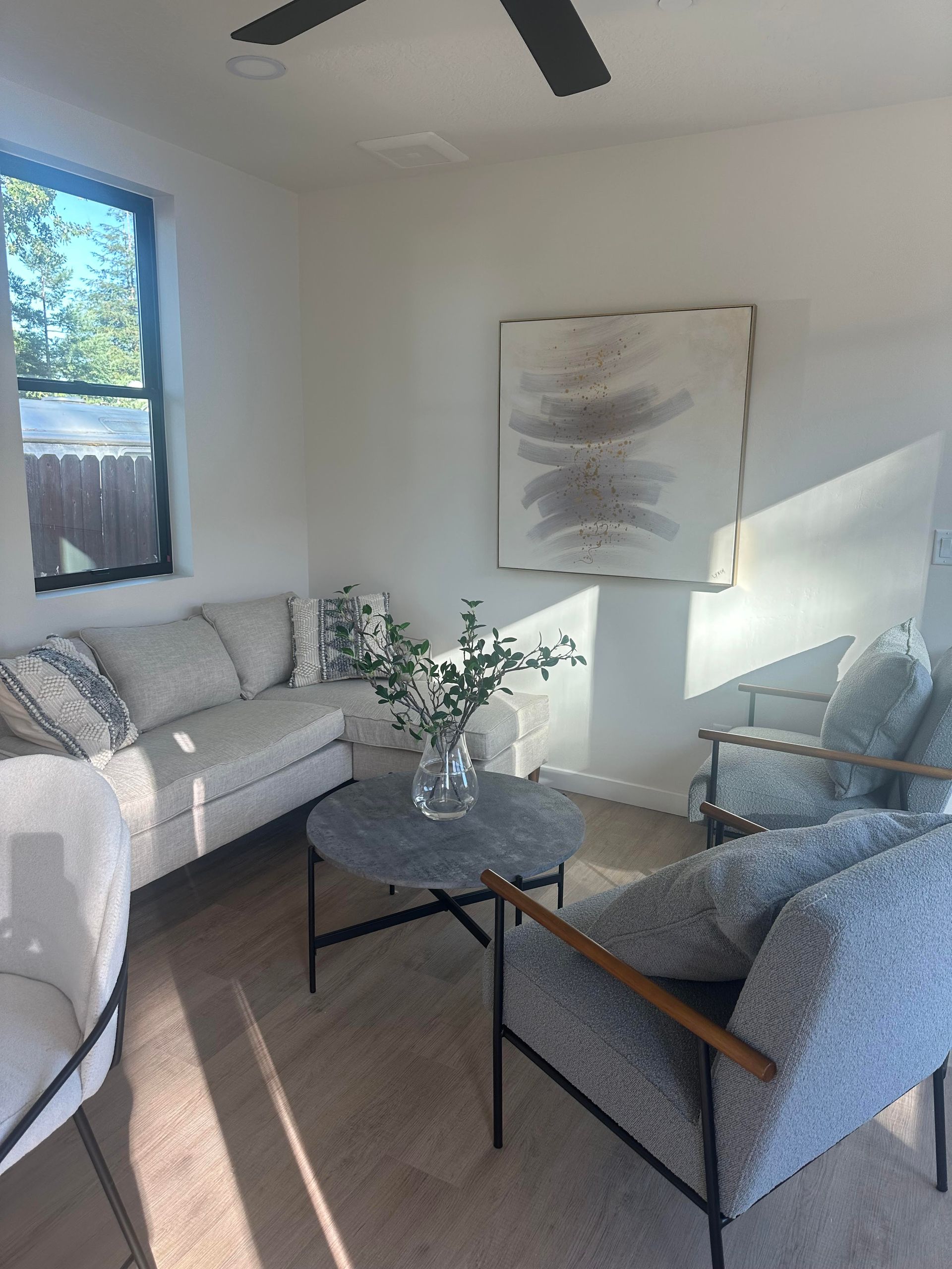 Perpetual Homes ADU: Living room with a light-colored sofa, gray armchairs, round coffee table, and abstract art.