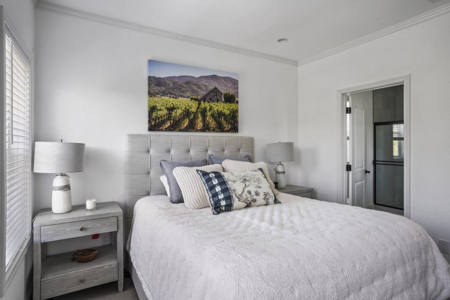 Perpetual Homes ADU: Bedroom with bed, nightstands, and landscape art. White walls, open door to a bathroom.