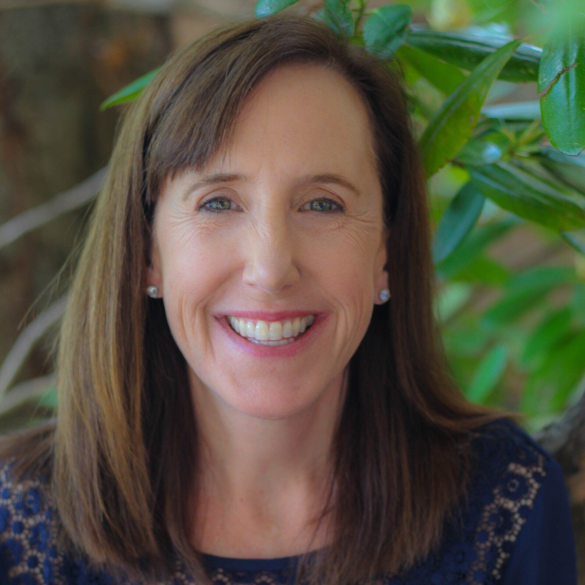 Beth McKnight, Perpetual Homes ADU. Woman with brown hair smiling, wearing a blue patterned top, with greenery in background.