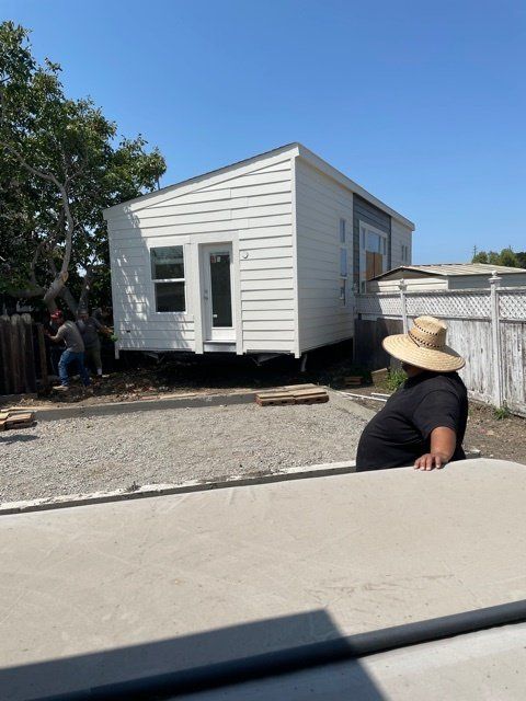 Perpetual Homes ADU: White tiny house on gravel, two people working on the side, one person in a hat looking on.