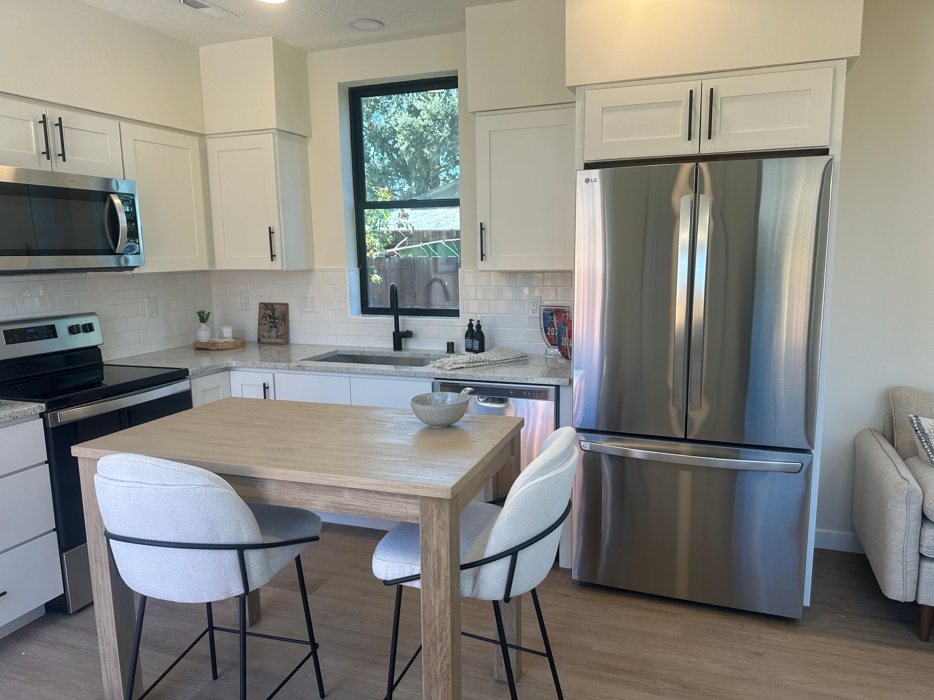 Perpetual Homes ADU: Modern kitchen with stainless steel refrigerator, white cabinets, and a wooden island with seating.
