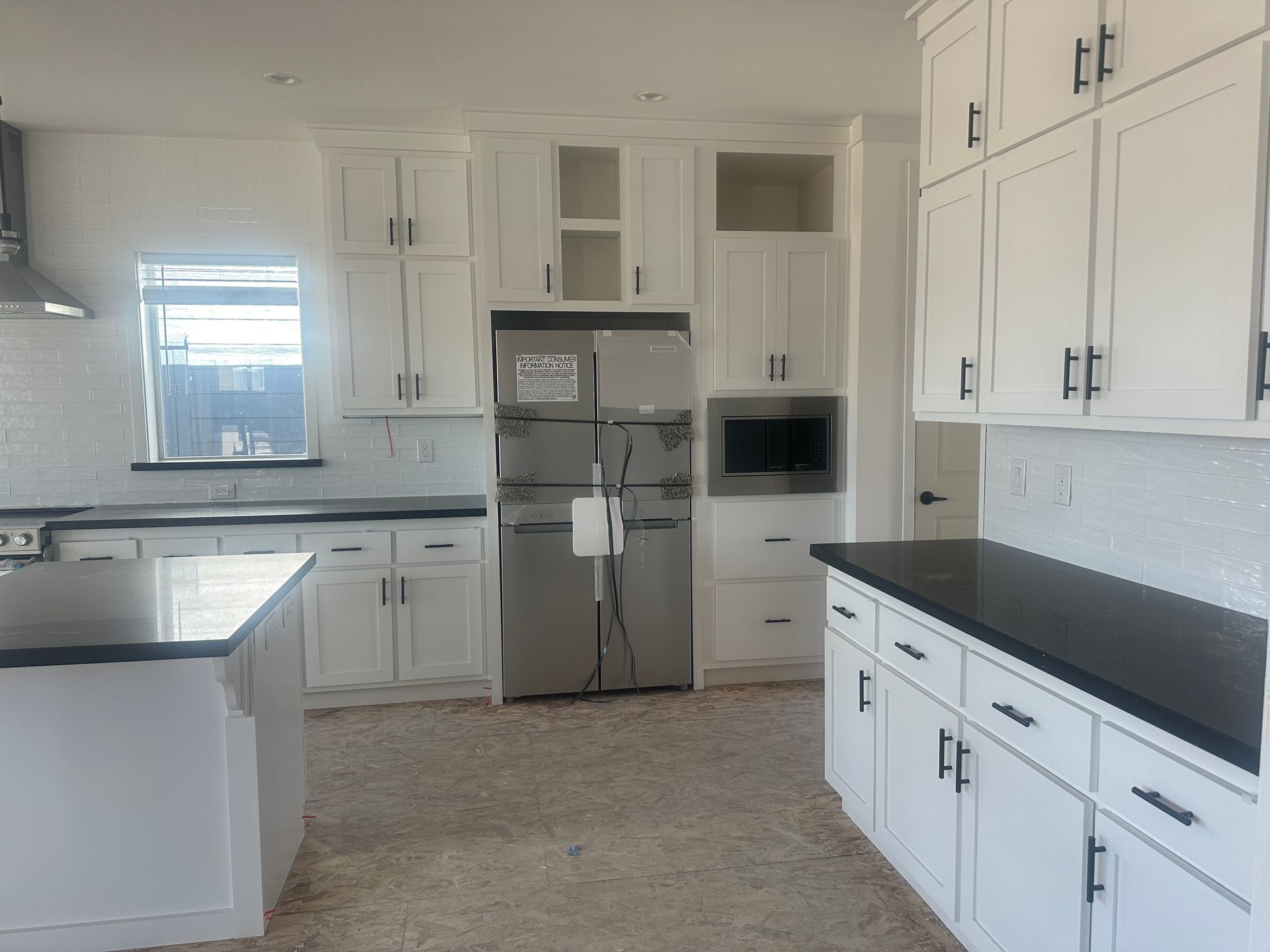 Perpetual Homes ADU: White kitchen with dark countertops, cabinets, stainless steel appliances, and a window.