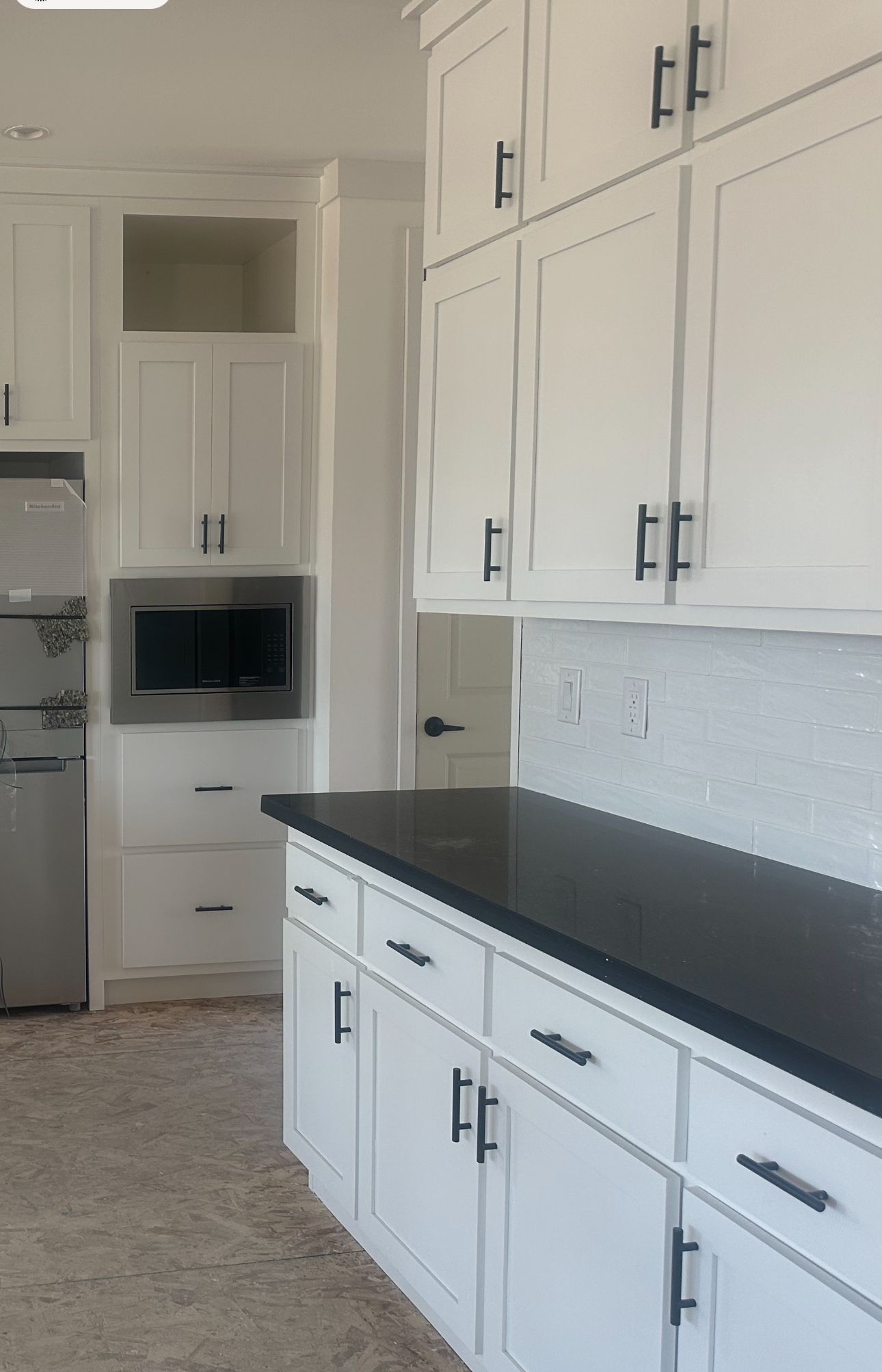 Perpetual Homes ADU: White kitchen cabinets with black countertops and hardware. Microwave built-in.