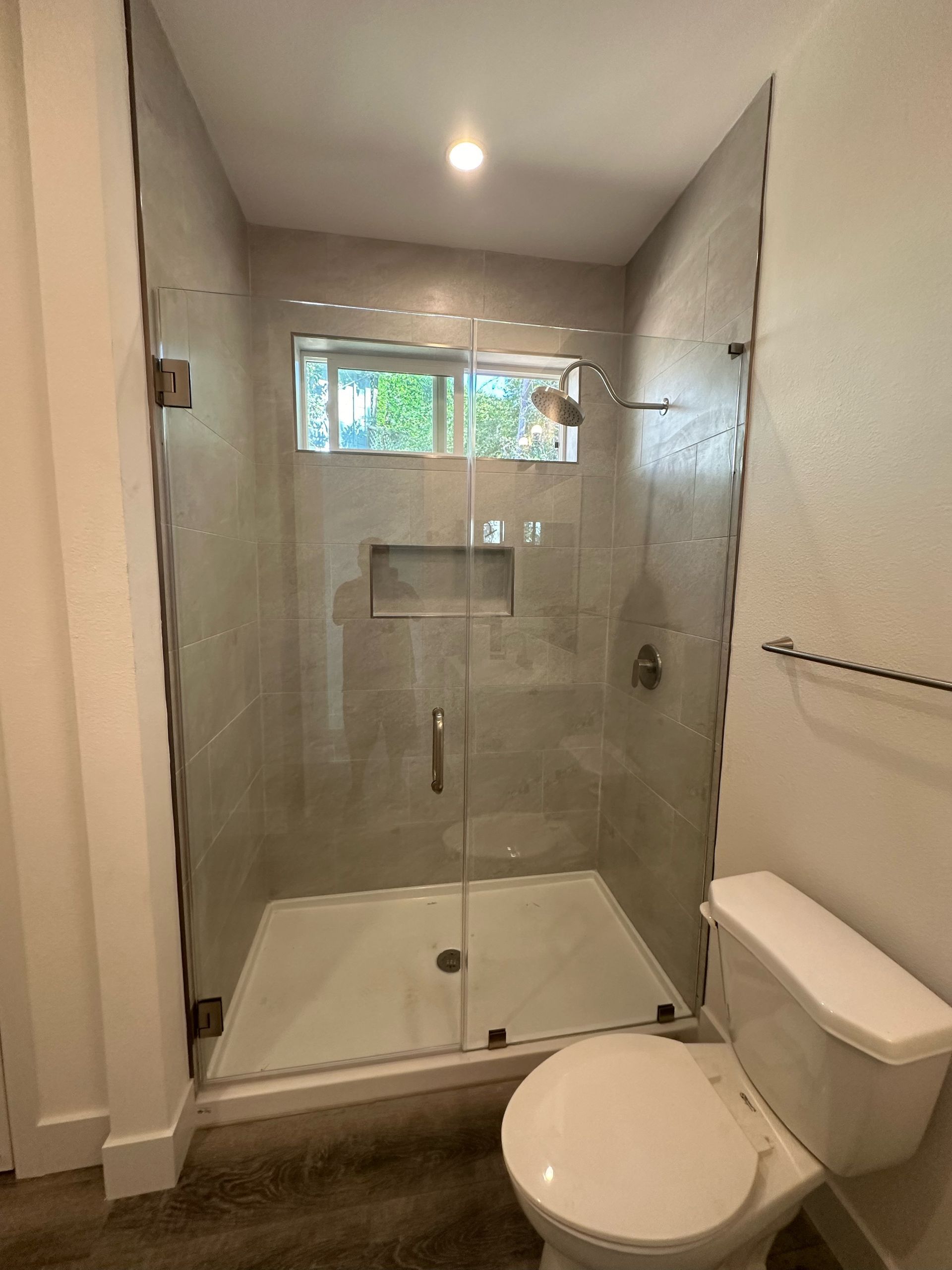 Perpetual Homes ADU: A modern bathroom with a glass shower enclosure, toilet, and a window.
