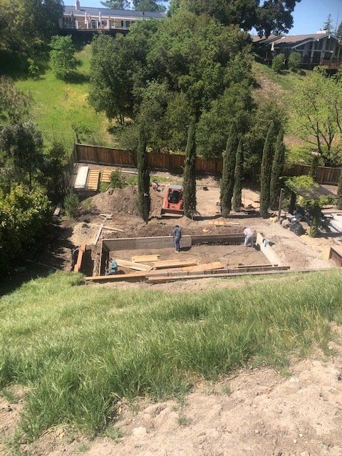 Perpetual Homes ADU: Pool construction on a hillside. Workers, excavator, dirt, and lumber are visible. 