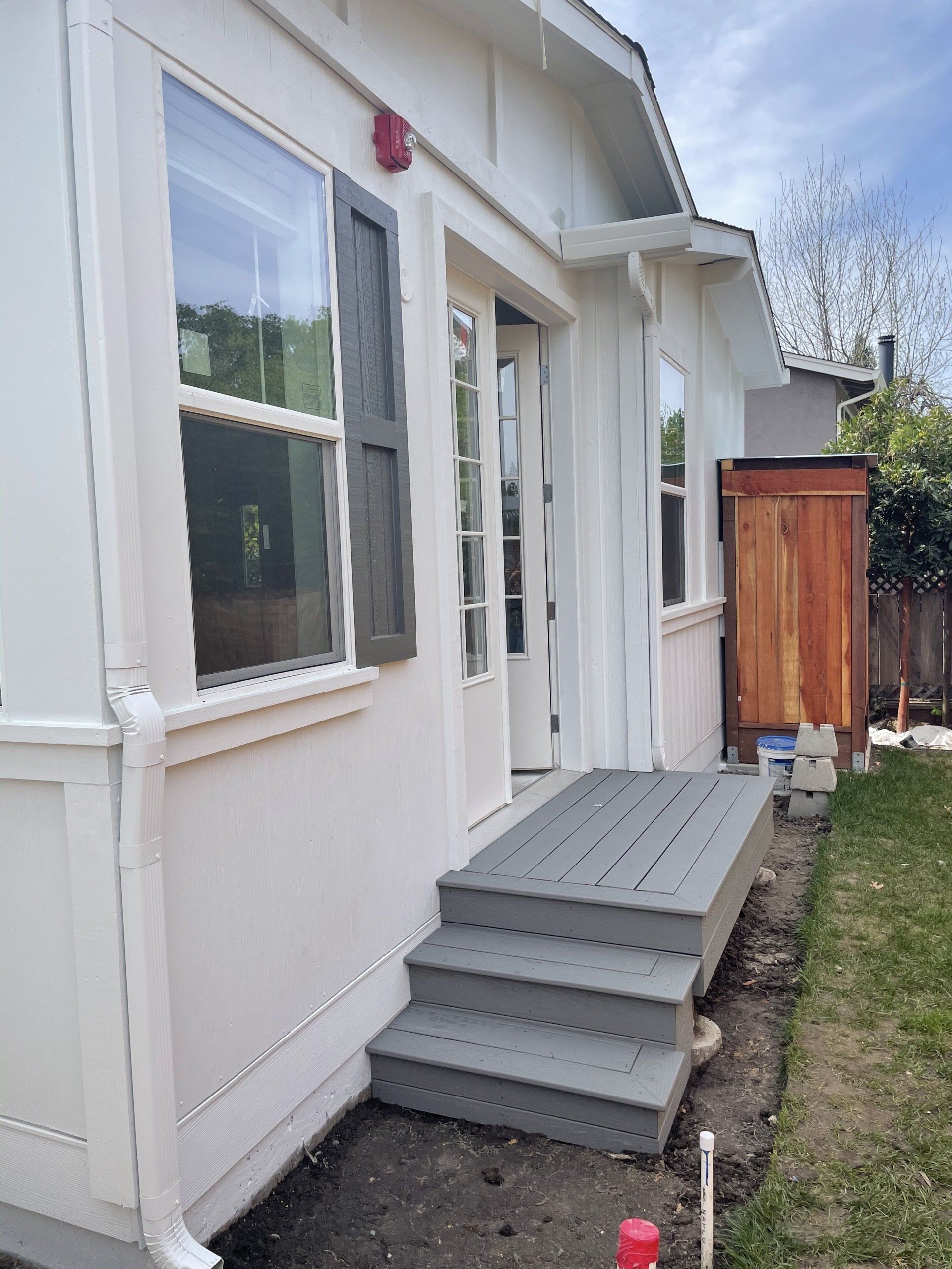 Perpetual Homes ADU: Exterior of a white house with grey deck steps and door. A brown water tank is visible.