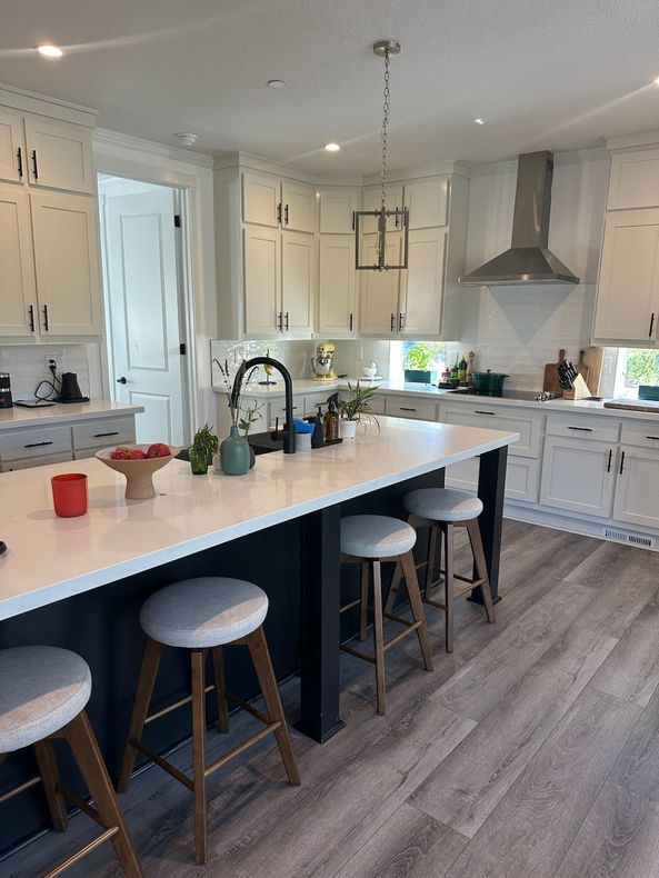 Perpetual Homes ADU: Kitchen with white cabinets, dark blue island, white countertops, and wooden stools.