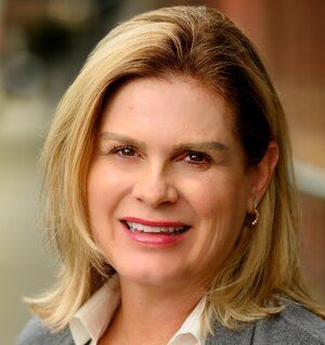 Katherine Anderson, Perpetual Homes ADU: Blonde woman smiles, wearing a gray blazer and white shirt; background is blurred.